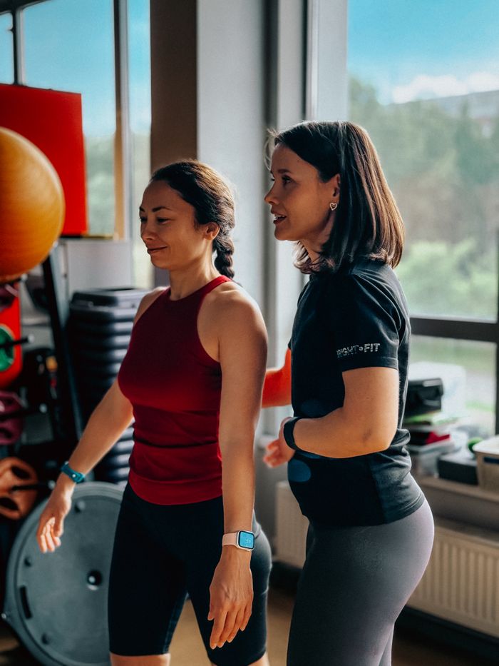 A female personal trainer guides a woman during a gym workout, promoting fitness and a healthy lifestyle.